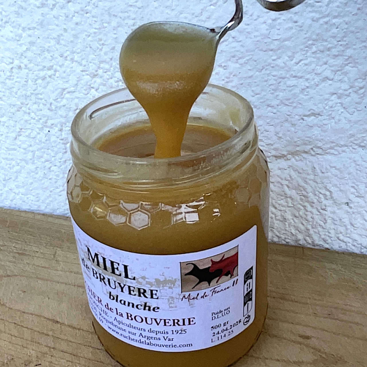 Geöffnetes Glas Baumheidehonig mit Löffel und herabfließendem Honig